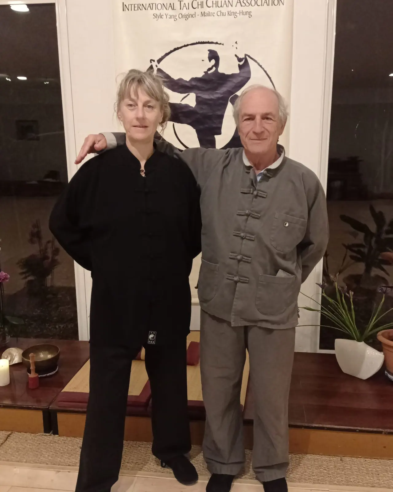 Catherine Mauguin et son maître de Tai Chi, en tenue, devant la bannière de l'International Tai Chi Chuan Association