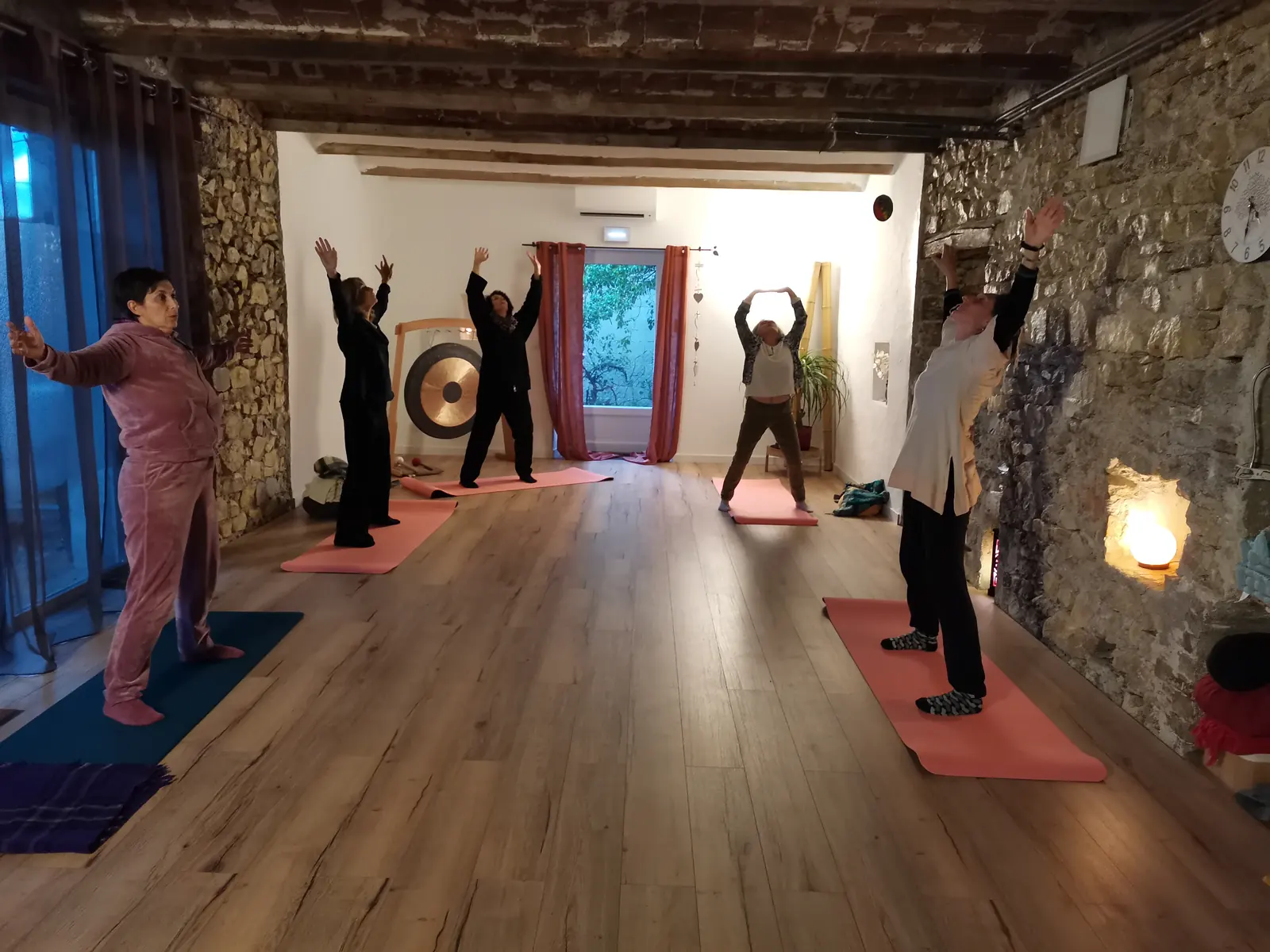 Cours collectif, bras levés, dans la salle aux murs de pierre et au gong