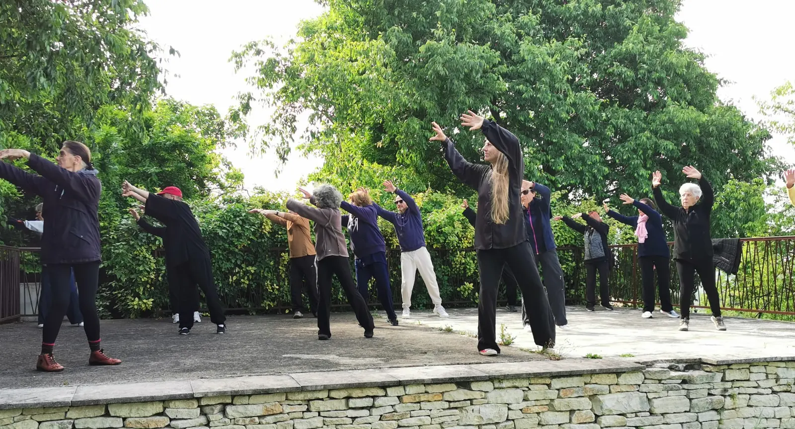 Pratique collective de Qi Gong sur une terrasse, au-dessus d'un muret de pierre