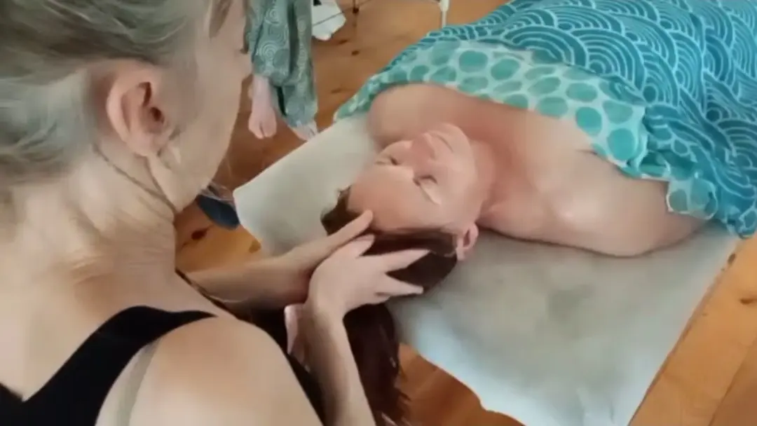Un soin crânien : les mains de la praticienne soutiennent la tête d'une personne allongée